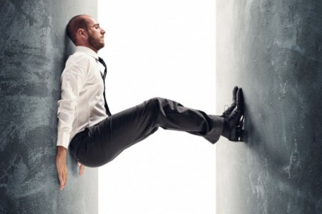 A businessman trapped suspended between two narrow walls, symbolizing being stuck in a routine and held back by limiting thoughts.