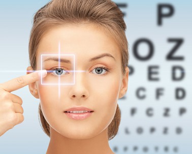 Woman checking her vision with an eye chart in the background, pointing to her focused eye.